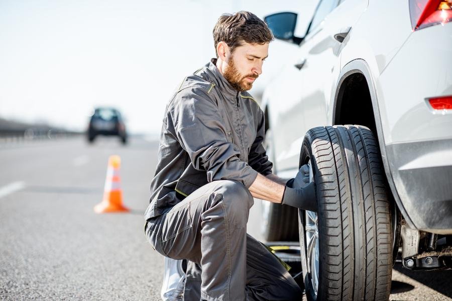 Tow truck operator changing a tire on the side of the road in Newmarket